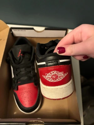 Air Jordan 1 Low röd/svart/vit - Säljer ett par Air Jordan 1 Low sneakers i rött, svart och vitt. Skorna har klassisk Jordan-logga på hälen, svart snörning och röd tåbox. Ovandelen är i läder och sulan är vit med röd yttersula. Perfekta för dig som gillar streetwear och ikoniska sneakers. Köpta i Japan för tre år sedan och använda max 5 gånger. Original kartongen har jag sparat.