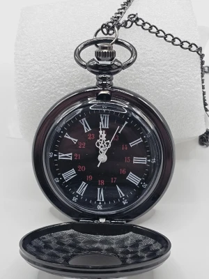 Svart fickur med kedja "klocka" - Stilrent svart fickur med klassisk kedja. Urtavlan har vita romerska siffror och röda 24-timmarsmarkeringar. Klockan har dekorativa visare och ett lock med cirkulärt mönster. Perfekt accessoar för dig som gillar vintage och retrostil.