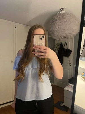 Ljusblå offshoulder topp med volang - Säljer en ljusblå offshoulder topp med volangdetalj över bröstet. Perfekt för dig som gillar en luftig och trendig stil. Toppen är ärmlös och har en loose passform som känns bekväm och snygg.