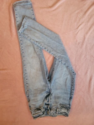 Ljusblå skinny jeans med hög midja - Säljer ett par ljusblå skinny jeans med hög midja och klassisk femficksdesign. Jeansen har dragkedja och knapp framtill samt bälteshällor. Perfekta för en avslappnad och trendig look.