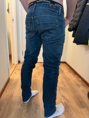 Dondup jeans - Säljer ett par blå slim fit jeans med snygga dragkedjedetaljer på bakfickorna och lätt slitning på ena låret. Jeansen har klassisk femficksdesign och smal passform som sitter tajt längs benen. Perfekta för en trendig och avslappnad stil.