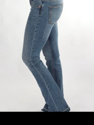 Blå bootcut jeans med låg midja - Snygga blå bootcut jeans med låg midja och klassiska fem fickor. Jeansen har en lätt tvättad look och är tillverkade i ett stretchigt denimtyg som sitter bekvämt. Perfekta för dig som gillar en retroinspirerad stil.