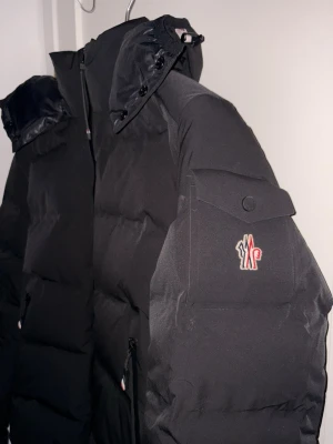 Moncler Grenoble - Säljer en svart pufferjacka från Moncler med avtagbar huva och dragkedja framtill. 