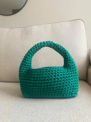 Grön virkad handväska - Cool handväska i grönt, virkat material med rundad form och breda handtag. Perfekt för dig som vill sticka ut med en unik accessoar. Väskan är handgjord och har en chunky look som känns trendig och modern.