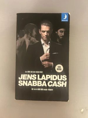 Snabba Cash av Jens Lapidus - En populär svensk kriminalroman av Jens Lapidus med svart omslag och stora vita bokstäver. Pocketutgåva från Månpocket med extra material. Omslaget har en stilren design med personer i kostym och festmiljö.