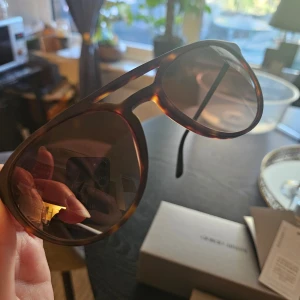 Solglasögon från Giorgio Armani - Säljer ett par snygga solglasögon från Giorgio Armani. De har en klassisk aviator-stil med en sköldpaddsmönstrad båge som ger en tidlös look. Glasen är mörka och ger bra skydd mot solen. Perfekta för både vardag och fest! Kommer med originalfodral och certifikat.