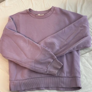 Lila sweatshirt - Säljer en mysig lila sweatshirt. Den har långa ärmar och ribbade muddar vid ärmslut och nederkant. Det finns en liten fläck på framsidan, men annars i bra skick. Perfekt för en avslappnad stil!