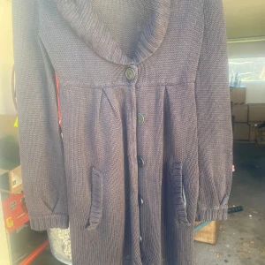 Mörk stickad kofta med knappar - Säljer en mysig mörk stickad kofta med stora knappar framtill. Den har långa ärmar och praktiska fickor. Perfekt för höst och vinter när du vill hålla dig varm och bekväm. Koftan är i bra skick och redo för en ny ägare!