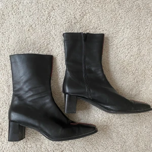 Stövlett stl 41 - Svarta italienska skinnstövletter i stl.41 med röda detaljer. Nästan helt oanvända. 6cm klack. 21cm från klack till slutet på skaft. (21+6cm totalt) Ny pris 1 750kr