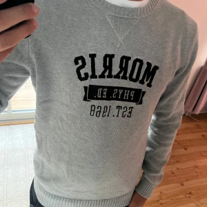 Grå tröja från Morris - Säljer en snygg grå tröja från Morris med tryck på framsidan. Den har långa ärmar och ribbade muddar vid ärmslut och nederkant. Tröjan är i storlek medium och i bra skick.