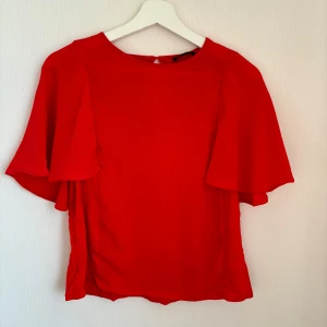 Röd topp från Zoul - Säljer en snygg röd topp från Zoul i storlek S. Toppen har korta ärmar och en liten knappdetalj i nacken. Har använts på julafton. 🤶 