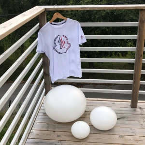 Vit t-shirt från Moncler - Säljer en snygg vit t-shirt från Moncler med ett stort broderat logotypmotiv på framsidan. T-shirten har korta ärmar och en normal passform. Perfekt för en avslappnad och stilren look! (Kvitto på sista bilden)