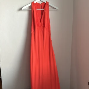 Orange långklänning från MNG - Orange långklänning från MNG (artnr 67009238) med djup v-ringning och ärmlös.  Perfekt för sommarens fester. Klänningen har en dragkedja i sidan för enkel påklädning. Materialet känns lätt och luftigt. Använd 1 gång på bröllop. 💒 