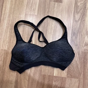 Svart sport-bh - Grå sport-bh med svart detalj. Den har justerbara axelband och en bekväm passform, perfekt för träning. Från trofé i storlek 70B!