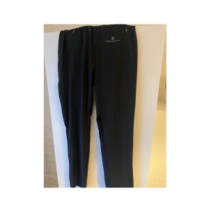 Svarta träningsbyxor från Ronhill - Säljer ett par svarta träningsbyxor/vindbyxor från Ronhill. Byxorna har en elastisk midja och är perfekta för löpning eller annan träning. De är tillverkade i ett lätt och bekvämt material.