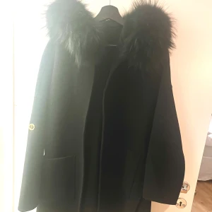 Svart kappa - Elegant svart kappa med lyxig pälsdetalj runt kragen. Perfekt för kyliga dagar och ger en sofistikerad look. Kappan har långa ärmar och en stilren design. Använd fåtal gånger, som ny. Priset kan diskuteras 