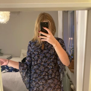 Blommig klänning med vida ärmar - Säljer en vacker blommig klänning i mörkblått med inslag av ljusblå och vita blommor. Klänningen har kortare ärmar som sedan går ner. Den har en fin passform och ett luftigt fall. Säljer då den ej kommer till andvändning. Som ny och nypris var 250kr för ett år sedan💗
