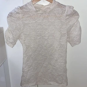 Vit spetsblus från Kappahl - Säljer en elegant vit spetsblus från Kappahl i storlek XS. Blusen har korta puff ärmar och ett vackert spetsmönster. Perfekt för att lyfta vilken outfit som helst. 