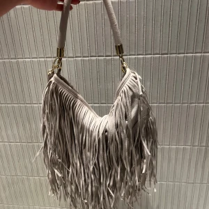  axelväska med fransar - Snygg beige axelväska med fransar som ger en bohemisk touch. Väskan har en bekväm axelrem och är perfekt för att addera lite stil till din outfit.