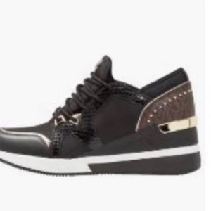 Svarta sneakers med gulddetaljer Mk - Stilrena svarta sneakers med gulddetaljer och snörning. Skorna har en modern design med en vit sula och bruna inslag på hälen.