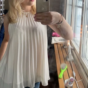 Vit ärmlös blus - Säljer en elegant vit blus med plisserad design. Passar både till jeans och kjol för en stilren look. Inga defekter. 