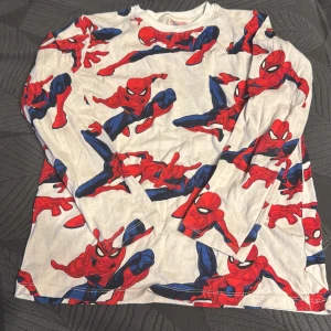 Vit långärmad tröja med Spiderman-motiv - Cool vit långärmad tröja med färgglatt Spiderman-motiv i rött och blått. Perfekt för alla superhjältefans! Storlek 134-140