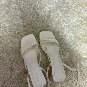 Vita sandaler med klack - Eleganta vita sandaler med smala remmar och fyrkantig tå. De har en stilren design med en låg klack, perfekt för sommarens alla tillfällen.