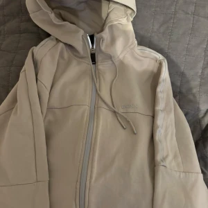 Beige huvtröja från BOSS - Snygg beige huvtröja från BOSS med dragkedja och justerbar huva. Perfekt för en avslappnad stil.