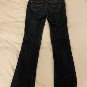 Mörkblå bootcut jeans från Lee - Snygga mörkblå bootcut jeans från Lee med klassisk femficksdesign. Jeansen har en lågmidjad passform och är perfekta för en avslappnad stil. De har en dragkedja och knapp framtill.