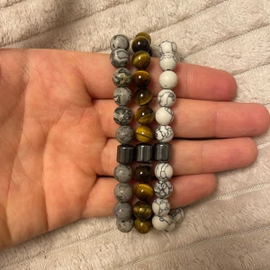 Set med tre pärlarmband - Snygga armband i set om tre med olika färger och mönster. Ett armband med grå marmorerade pärlor, ett med vita pärlor med svarta ådringar och ett med bruna tigeröga-pärlor. Alla armband har en metallisk detalj i mitten.