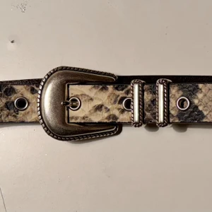 Sheriff belt HOPE faux snake 80 cm  - Läderbälte fr HOPE. 2,5 cm brett Western spänne och metall detaljer Faux snake mönstrat beige/svart Vissa repor på metallen men inget som stör. Vintage look.  Läder intakt. Målade kanter. Fint skick.  67 cm till första hålet 95 cm till sista hålet. 