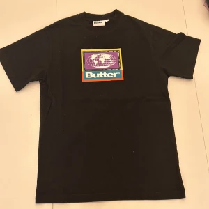 Svart t-shirt från Butter - Snygg svart t-shirt från Butter med ett färgglatt tryck på bröstet. Skriv om ni har frågor.