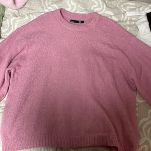 Rosa stickad tröja från 157 - Mysig rosa stickad tröja från 157. Perfekt för kyliga dagar med sin bekväma passform och ribbade detaljer vid ärmslut och nederkant. Enkelt att matcha med olika outfits.