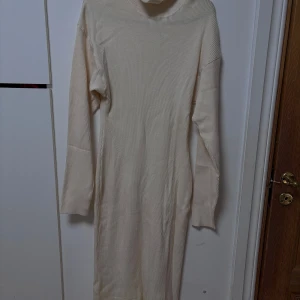 Beige ribbad långklänning - Snygg beige långklänning med ribbad struktur och långa ärmar. Perfekt för en stilren och bekväm look. Klänningen har en hög krage som ger extra värme och stil. Använt endast under nyår 2023, känner mig obekväm av polon.