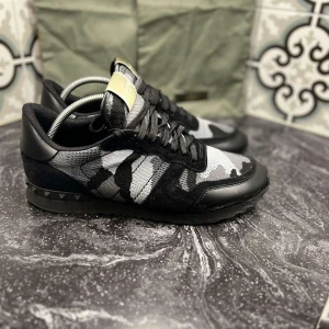 Valentino Rockrunner  - Snygga Valentino Rockrunner sneakers i svart och grått med ett coolt camouflage-mönster. Skorna har snörning och är dekorerade med nitar på sulan. Perfekta för vintern för endast 2999kr