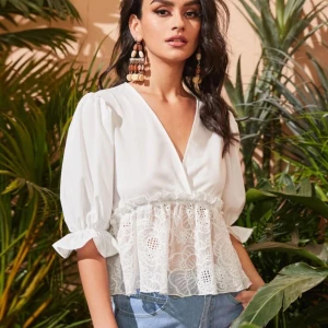 Vit blus med spetsdetaljer - Säljer en elegant vit blus med v-ringning och spetsdetaljer i midjan. Blusen har trekvartsärmar med volang och knytband vid ärmsluten. Perfekt för en stilren look.