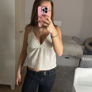 Vit sommar linne - Säljer en söt vit topp med smala axelband och volangdetaljer. Toppen har en lätt och luftig design, perfekt för varma dagar.