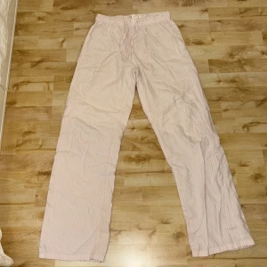 Randiga byxor från Gina Tricot - Säljer ett par bekväma och stilrena randiga byxor från Gina Tricot. Byxorna är ljusa med ett diskret randigt mönster och har en avslappnad passform med snörning i midjan. Perfekta för en avslappnad look.