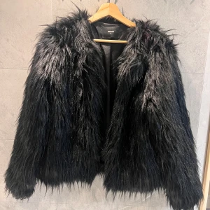 Svart pälsjacka från Bik Bok - Säljer nu min älskade fest pälsjacka från BikBok med långa ärmar och fluffig textur. Passar till många olika outfits. Som man kan se på bilderna är varan lite defekt, med röd färg vid axeln samt lite bränd vid en jackärmen. (Vet inte hur Plick fungerar riktigt, men pris kan diskuteras)