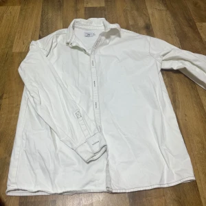 Vit långärmad skjorta - Klassisk vit långärmad skjorta med knappar. Perfekt för en stilren look. Skjortan har en normal passform och är tillverkad i ett mjukt material. Priset går att diskuteras 