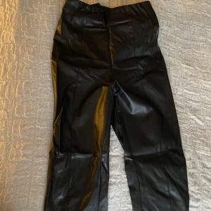 Svarta byxor från H&M - Snygga svarta byxor i syntetmaterial från H&M. De har en hög midja och en stilren design som passar perfekt för en trendig look. Byxorna har en rak passform. 