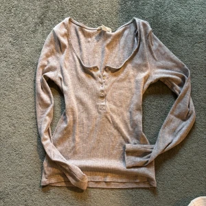 Grå ribbad långärmad topp - Säljer en stilren grå ribbad topp med långa ärmar och knappar framtill. Perfekt för en avslappnad look. Passar bra till jeans eller kjol.