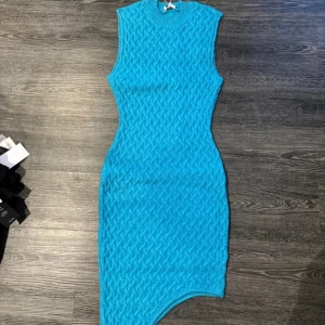 Blå stickad klänning - Snygg blå stickad klänning med asymmetrisk nederkant. Den är ärmlös och har en tight passform som framhäver figuren. Perfekt för en trendig look.