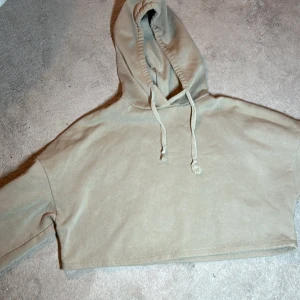 Beige croppad hoodie från Gina Tricot - Säljer en beige croppad hoodie från Gina Tricot. Den har en justerbar huva med dragsko och långa ärmar. Perfekt för en avslappnad stil. Hoodien ha även en mjuk insida!!