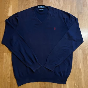 Ralph lauren tröja - Säljer en stilren mörkblå tröja från Ralph Lauren med v-ringning och det klassiska röda logotypbroderiet på bröstet. Skick: 9/10. Materialet är bomull, och perfekt som ett skönt o snyggt lager under jackan nu under vintern. Storlek: L. Mvh Carl
