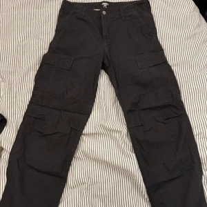Svarta cargobyxor från Carhartt WIP - Säljer ett par svarta cargobyxor från Carhartt WIP. Byxorna har flera praktiska fickor och en knapp med Carhartt-logga. Perfekta för en avslappnad stil.