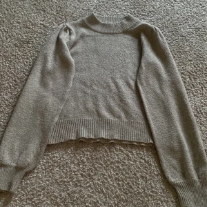 Beige/grå stickad tröja - Mysig beige stickad tröja med ribbade muddar och rund hals. Perfekt för kyligare dagar.