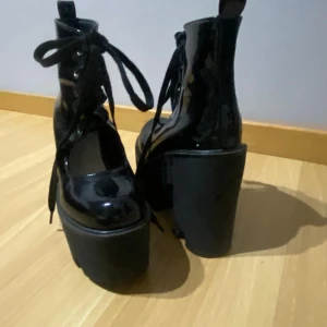 Svarta platåstövletter med snörning - Snygga svarta platåstövletter i syntetmaterial med hög klack och snörning framtill. Perfekta för att ge extra höjd och stil till din outfit.