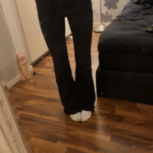 Svarta bootcut jeans - Snygga svarta bootcut jeans med hög midja. Perfekta för en stilren look. De har en klassisk design med dragkedja och knappar framtill.