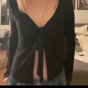 Svart långärmad topp från Gina Tricot - Säljer en svart långärmad topp från Gina Tricot med knytning framtill. Perfekt för en stilren look och kan enkelt matchas med olika outfits.